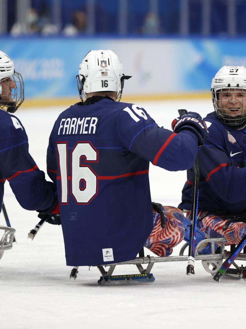 Three players in full Para ice hockey gear celebrating a goal with a smile.